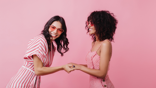 Two friends laughing and holding hands in matching pink outfits