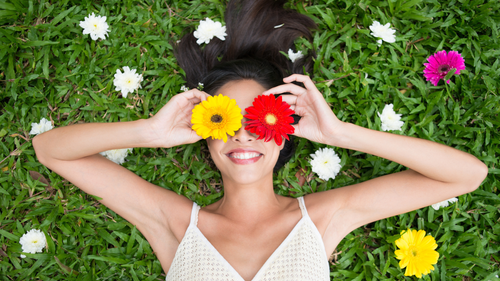 Woman lying in grass holding yellow and red gerbera daisies over her eyes