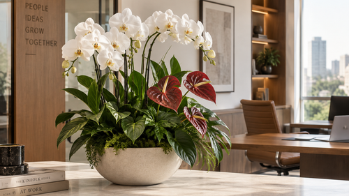 White orchids and red anthuriums in a white bowl planter on an office table.