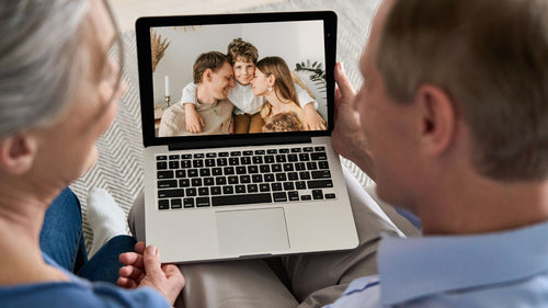 Grandparents video calling their son's family, shown smiling together on a laptop