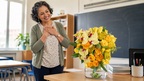 Yellow rose and orchid bouquet with ranunculus in a glass vase on a teacher's desk